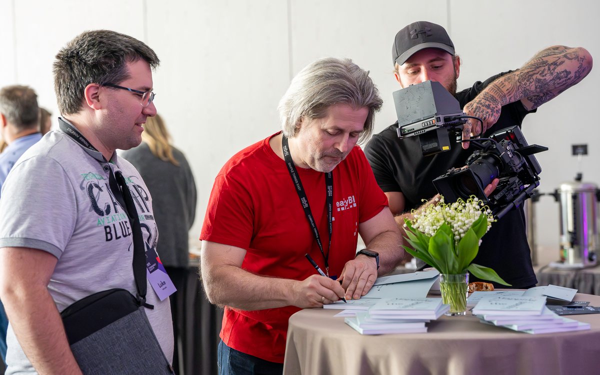 An eazyBI team member signing a book while a camera operator films