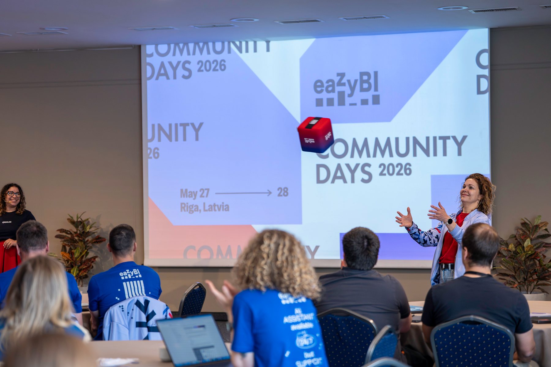 Host throwing the eazyBI cube on stage in front of the Community Days 2026 slide